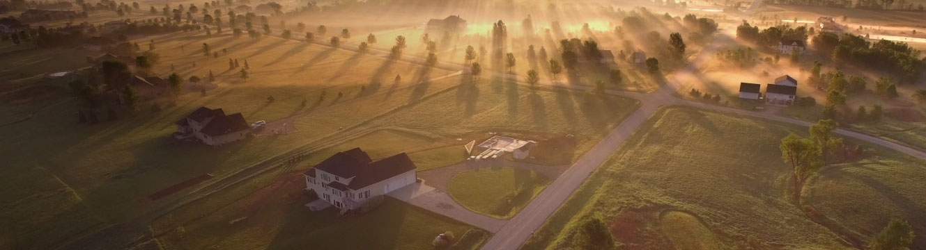 An aerial view of a rural community with the rising sun shining through fog.